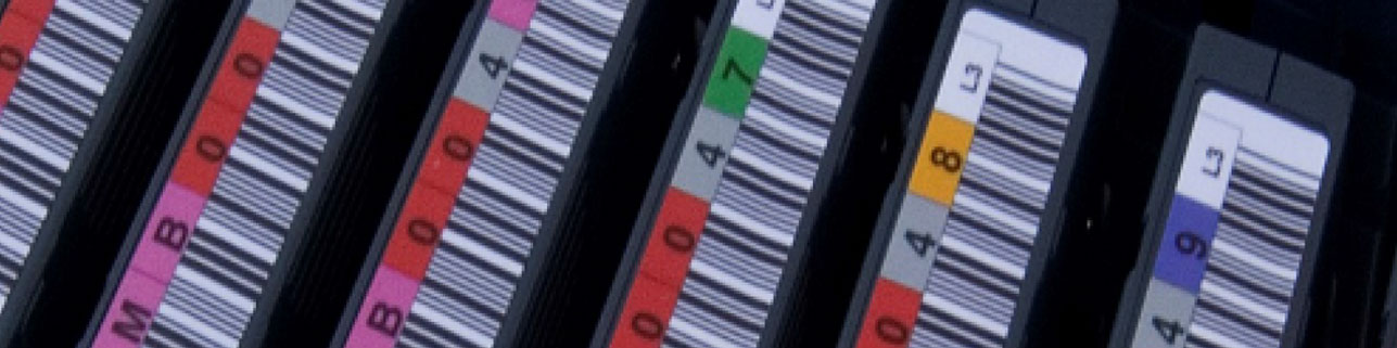 A series of data storage tape cartridges with colored barcode labels placed neatly on each of them.